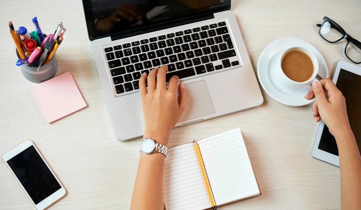 A laptop on a wooden desk, displaying the logos of Telus International AI, Appen, and Lionbridge. A person's hands are visible on a keyboard, suggesting remote work.